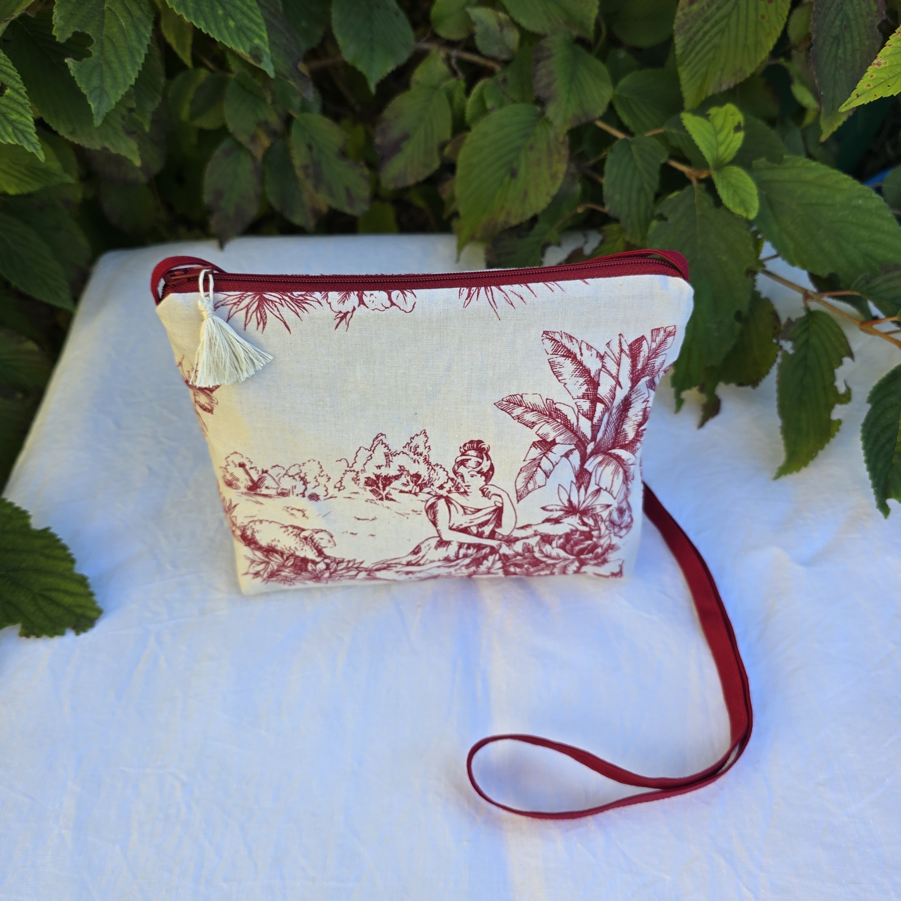 Pochette avec bandouli&egrave;re en tissu toile de Jouy bordeaux et &eacute;cru agr&eacute;ment&eacute;e d'un pompon