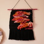 Suspension tissage mural d'inspiration florale en laines et coton de couleurs roses sur noir aux longues franges