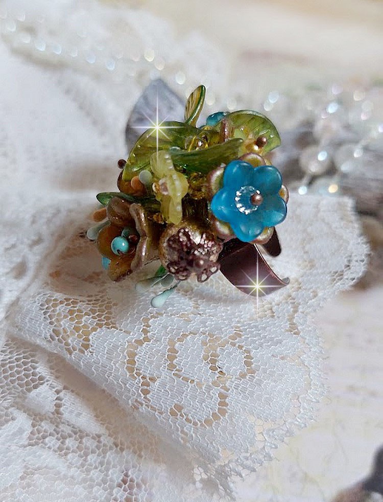 Bague Cézanne montée avec des petites fleurs lucites peintes à la main à laquelle s’ajoute des feuilles, cristaux, perles, étamines, grosses rocailles, perles nacrées et métal sur une bague en Laiton