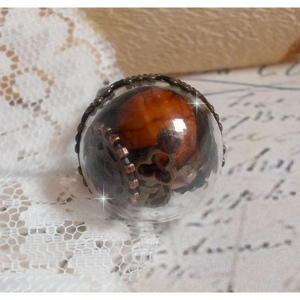 Bague Majest&eacute; Steampunk aux rouages m&eacute;caniques &agrave; laquelle s&rsquo;ajoute une cl&eacute; et un strass de couleur Siam et un strass en verre Dor&eacute;. Le tout est mis sous un globe en verre sur une bague r&eacute;glable laiton