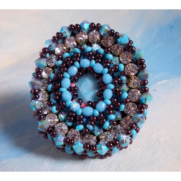 Na&iuml;ade ring broderet med en turkisbl&aring; harpiks og en krystalcabochon, et smukt spil af lys.