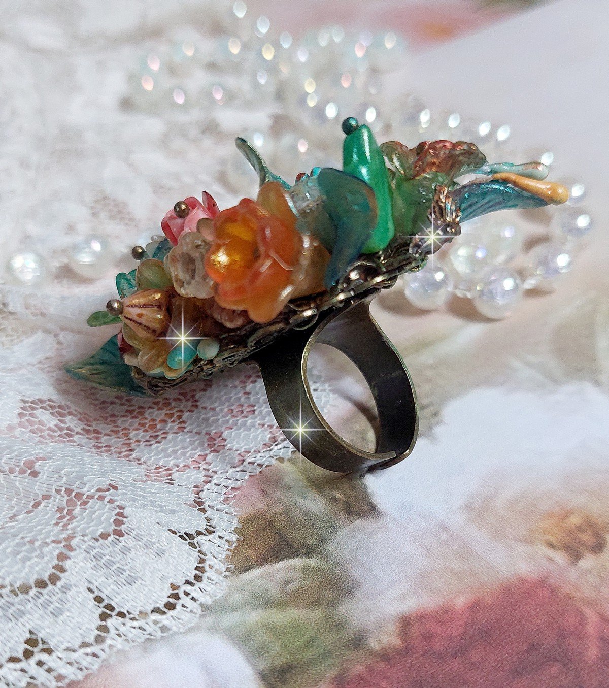 Bague Patiflo d&rsquo;une composition florale cr&eacute;&eacute;e avec des cristaux, fleurs en R&eacute;sine, perles, clochettes, pens&eacute;es, boutons de rose en Verre, estampes et coupelles. Le tout est mont&eacute; sur une bague estampe