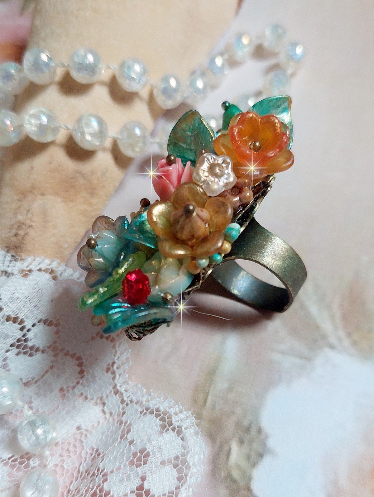 Bague Patiflo d&rsquo;une composition florale cr&eacute;&eacute;e avec des cristaux, fleurs en R&eacute;sine, perles, clochettes, pens&eacute;es, boutons de rose en Verre, estampes et coupelles. Le tout est mont&eacute; sur une bague estampe