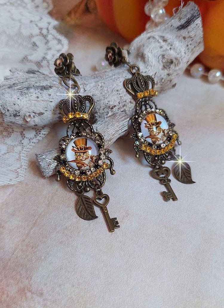 BO Chatibo Steampunk montées avec cabochons ronds en verre représentant un chat chapeauté Haute de Forme Orange. Strassées avec une couronne, breloques clés et feuilles. Montées sur clips Bronze