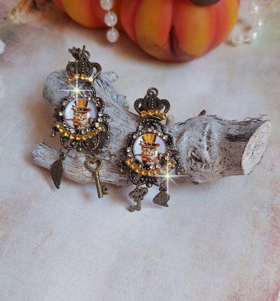 BO Chatibo Steampunk mont&eacute;es avec cabochons ronds en verre repr&eacute;sentant un chat chapeaut&eacute; Haute de Forme Orange. Strass&eacute;es avec une couronne, breloques cl&eacute;s et feuilles. Mont&eacute;es sur clips Bronze