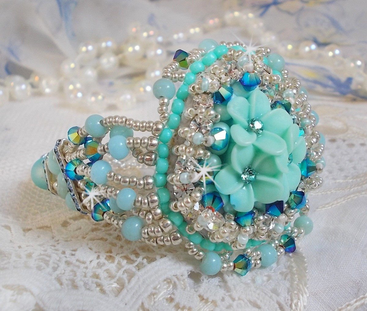 Bracelet Blue Flowers Haute-Couture brodé avec des Cristaux de Swarovski, un cabochon en résine, des perles rondes en satin, des rocailles avec une chaînette et un fermoir en Argent 925/1000