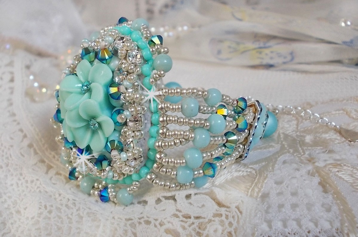 Bracelet Blue Flowers Haute-Couture brodé avec des Cristaux de Swarovski, un cabochon en résine, des perles rondes en satin, des rocailles avec une chaînette et un fermoir en Argent 925/1000