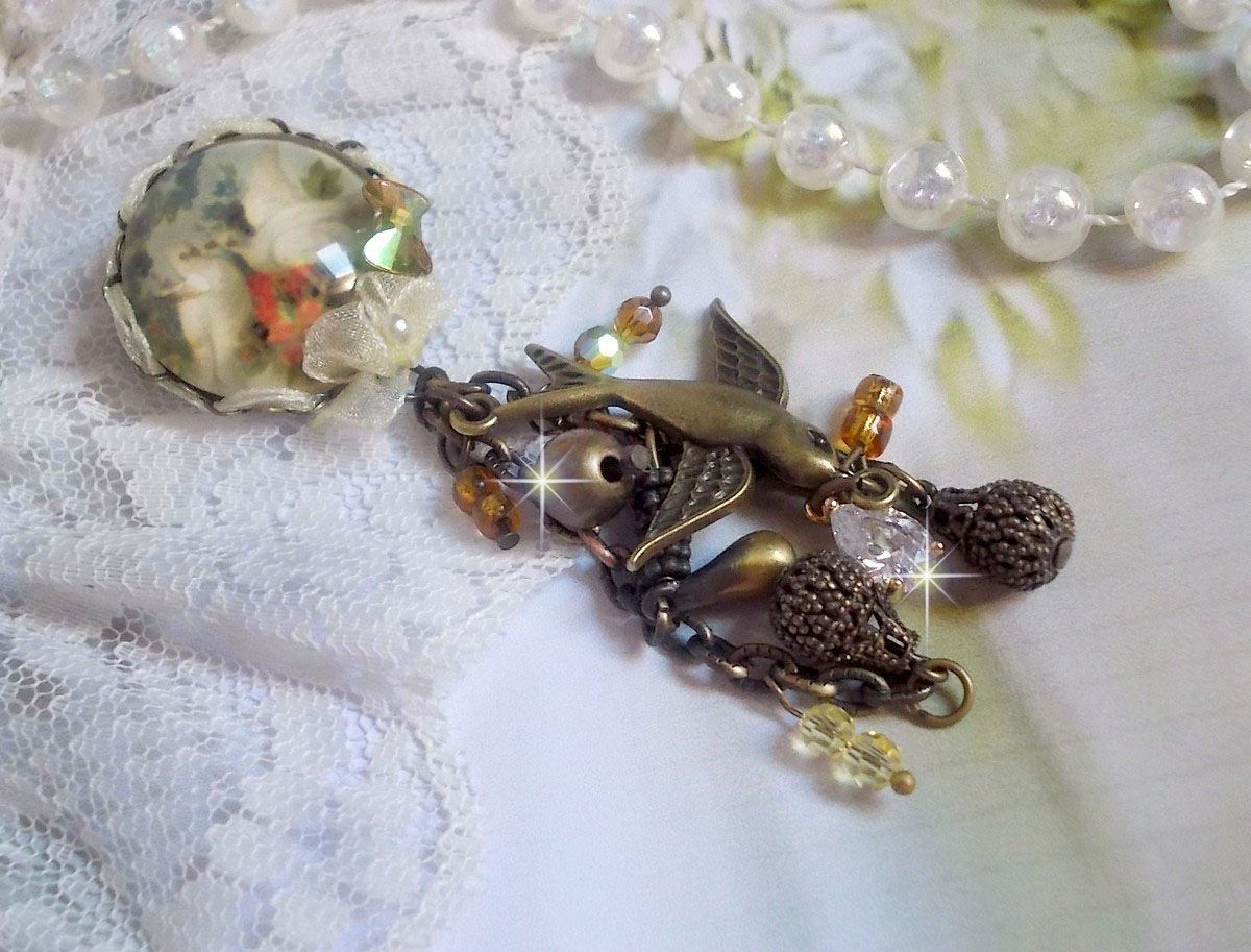 Broche Colombes aux plumages blancs avec des breloques filigranées gouttes et lisses, perles rondes et nœud en cristal, ruban organza crème, pendentif plaqué or avec un zircon sur une broche en métal