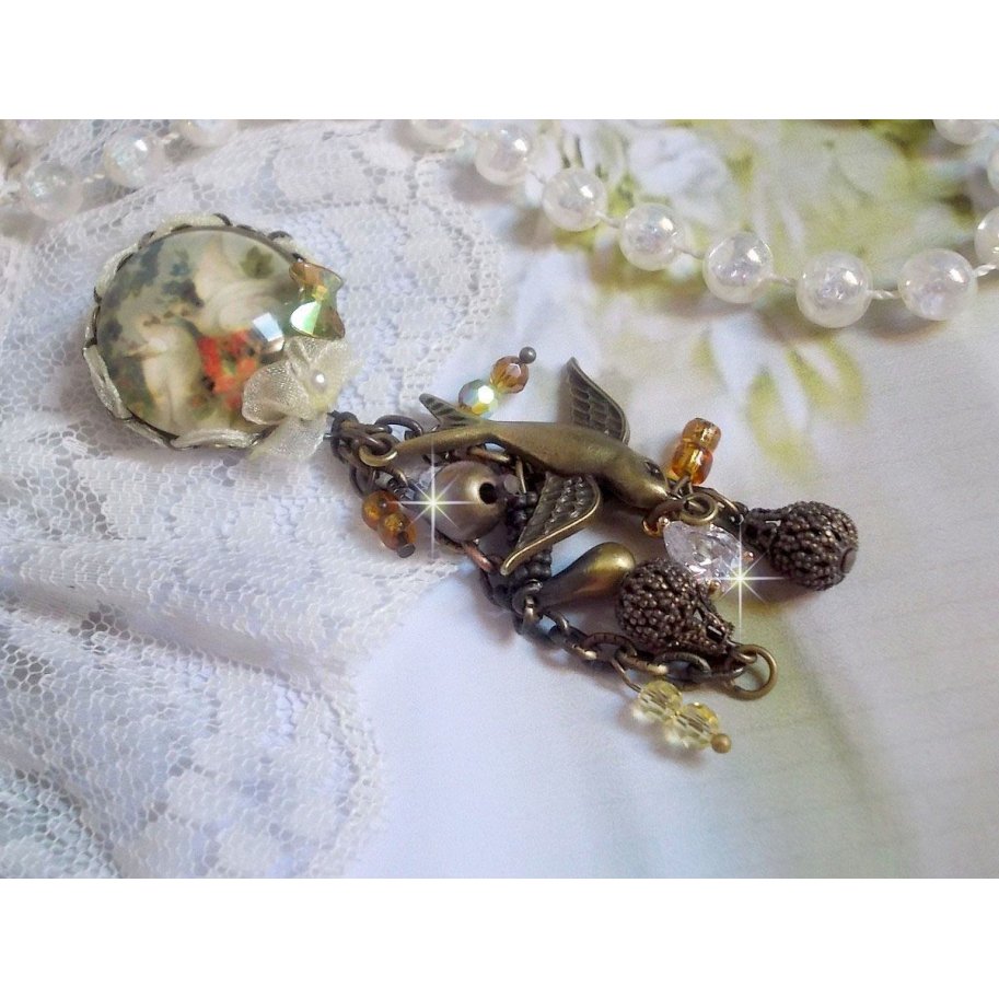 Broche Colombes aux plumages blancs avec des breloques filigranées gouttes et lisses, perles rondes et nœud en cristal, ruban organza crème, pendentif plaqué or avec un zircon sur une broche en métal