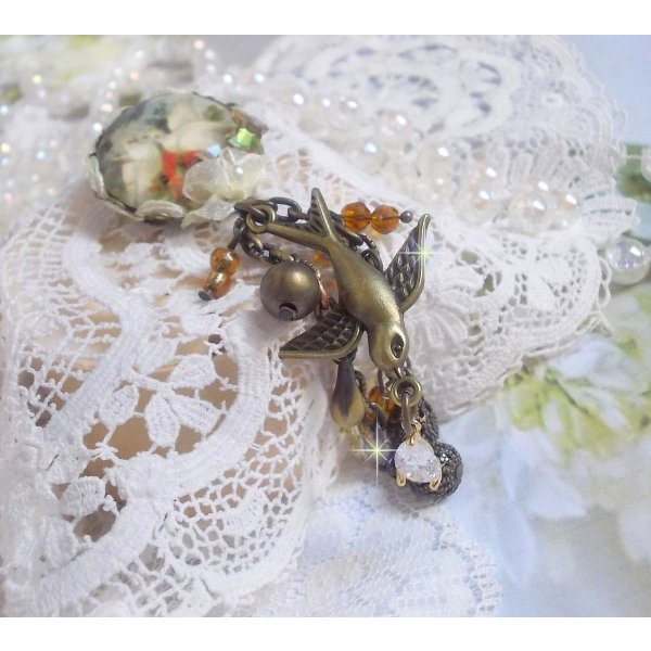 Broche Colombes aux plumages blancs avec des breloques filigran&eacute;es gouttes et lisses, perles rondes et n&oelig;ud en cristal, ruban organza cr&egrave;me, pendentif plaqu&eacute; or avec un zircon sur une broche en m&eacute;tal