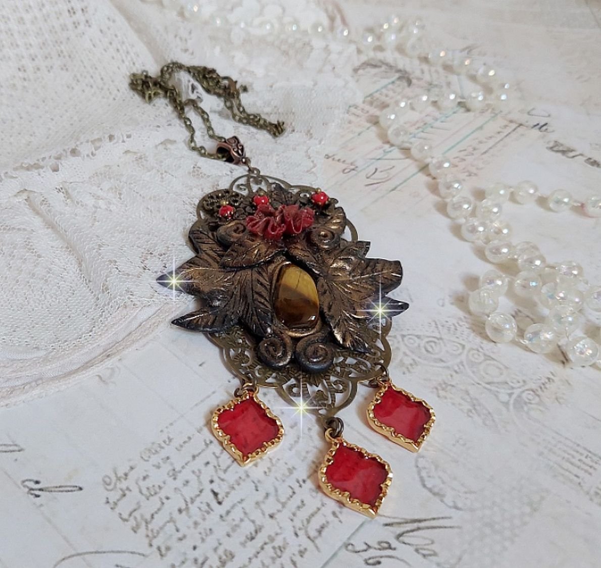 Pendentif Mélodie avec un cabochon Œil de tigre orné de perles en Jade Rouge veiné de Noir sur fleurs 5 pétales et estampes montés sur une chaîne bronze. Les pendants sont en résine époxy Rouge